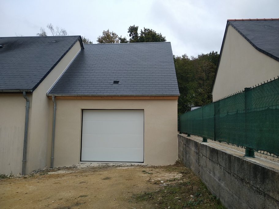 Photo d'un garage avec une porte de parking blanche et une toiture traditionnelle de la région.