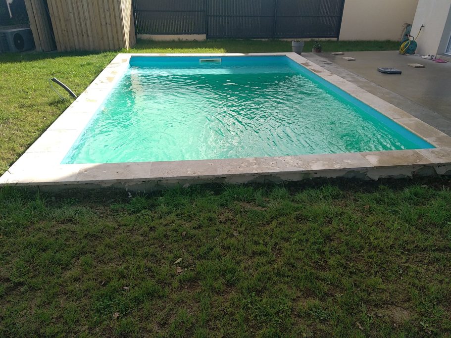 Photo d'une piscine creusée avec margelle en travertin 