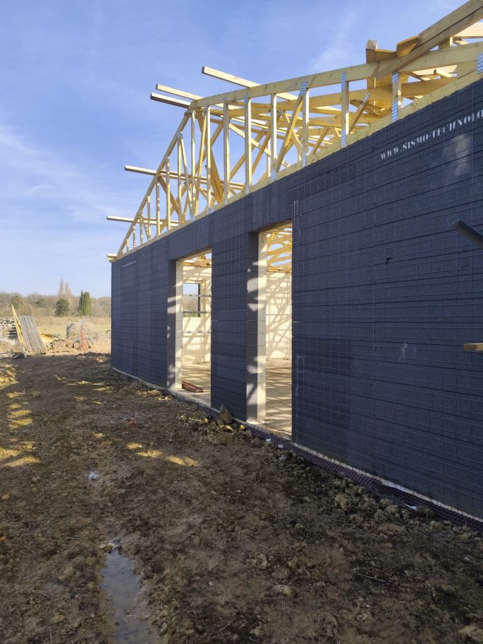 Photo d'un mur avec les plaquettes sismo apparente et de la charpente en cours d'installation