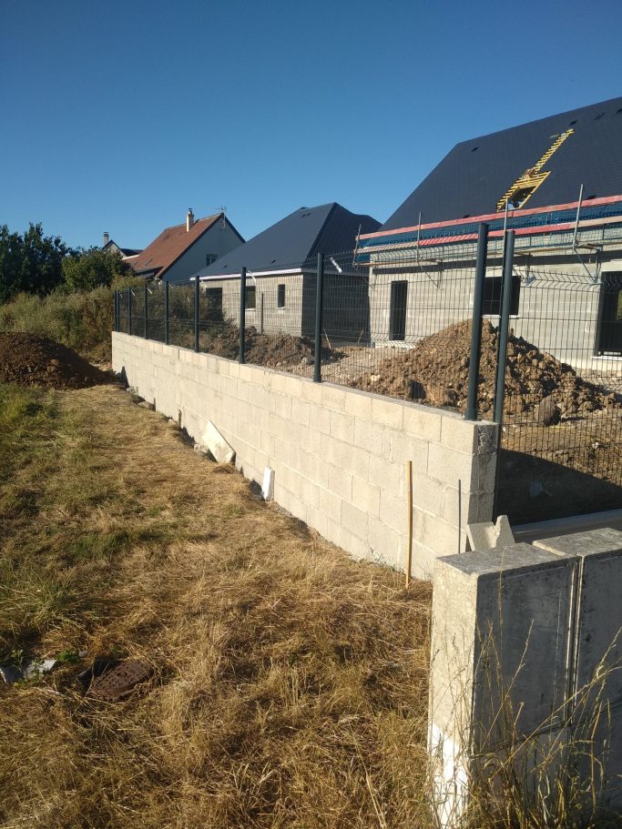 Photo des murs en parpaing et de la mise en place du grillage rigide avec la maison en fond 