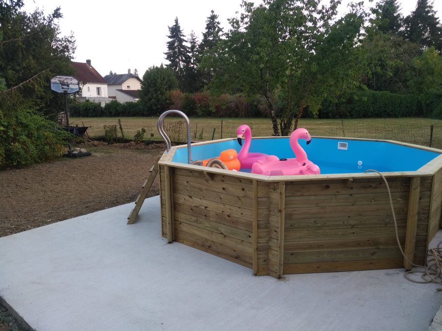 Photo d'une terrasse bétonnée avec une piscine en bois hors sol, et des bouées flament roses